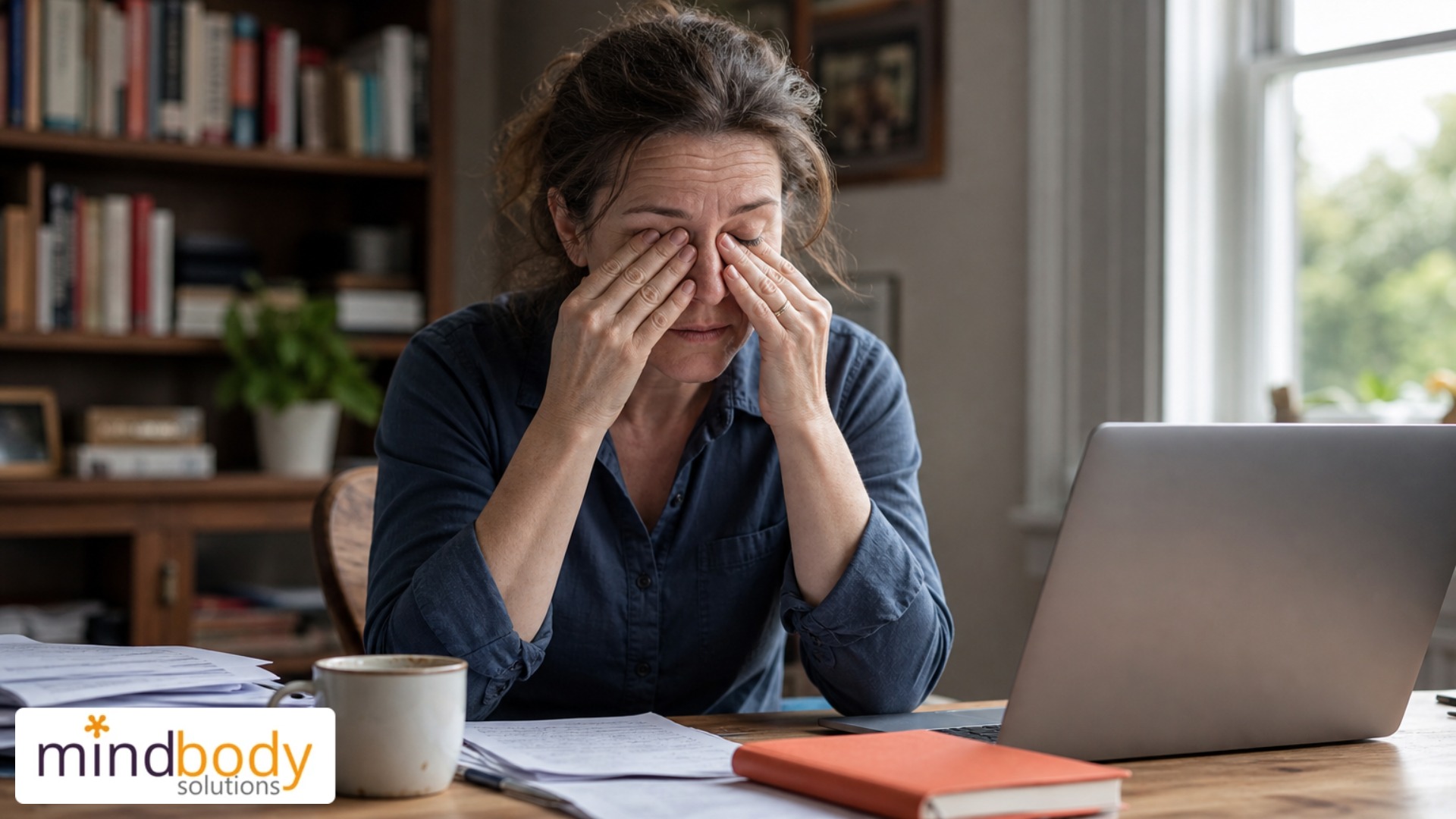 Tired woman rubbing eyes at desk illustrating fatigue and mental fog symptoms